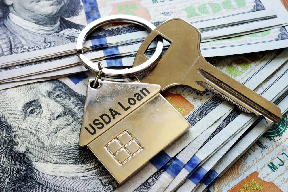 Keys with a house keychain that says USDA Loans on top of $100 bills