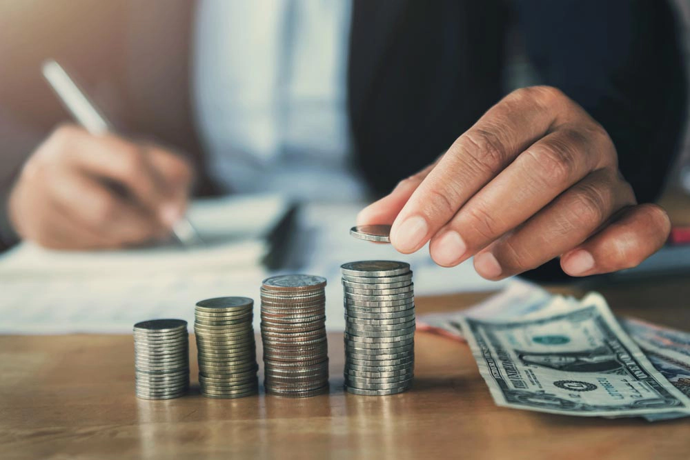 Business owner working on accounting books with a stack of coins and dollar bills in front of him