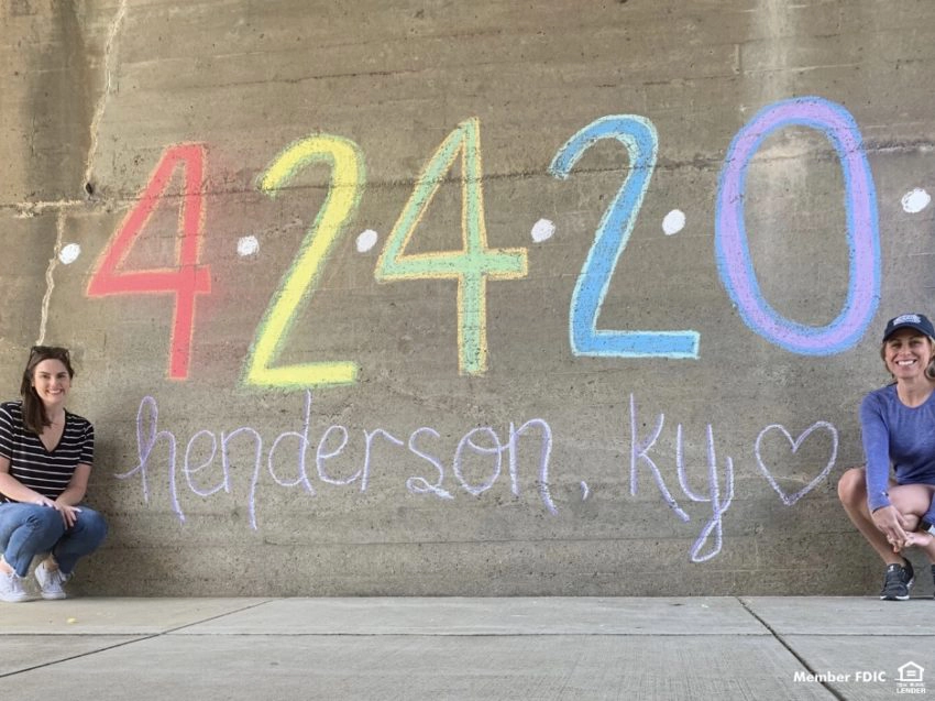 Two people next to a wall with writing in chalk: 4.24.20 Henderson KY"