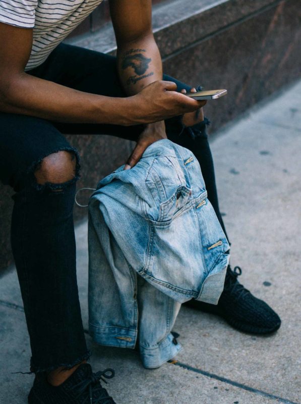 Many with tattoo looking at smartphone, holding jean jacket.