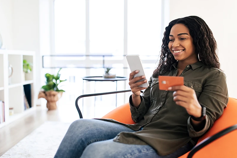 Woman holding debit card looking at mobile phone