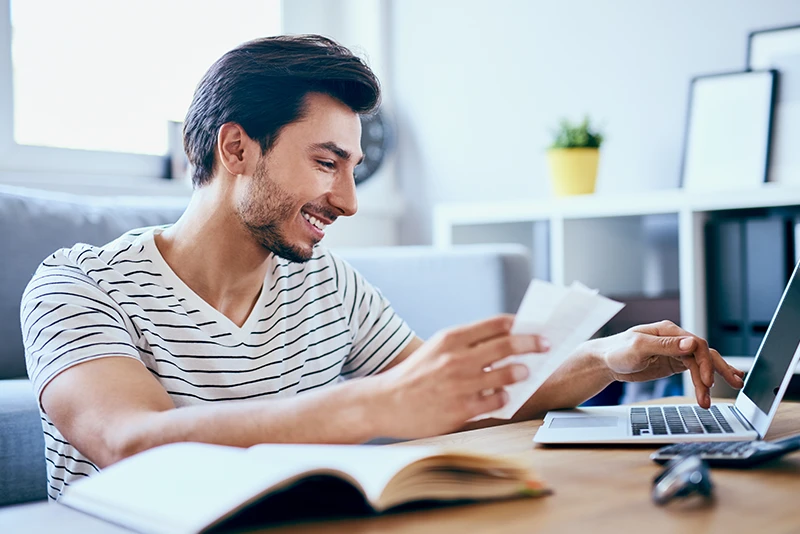 Man holding receipts and typing on laptop