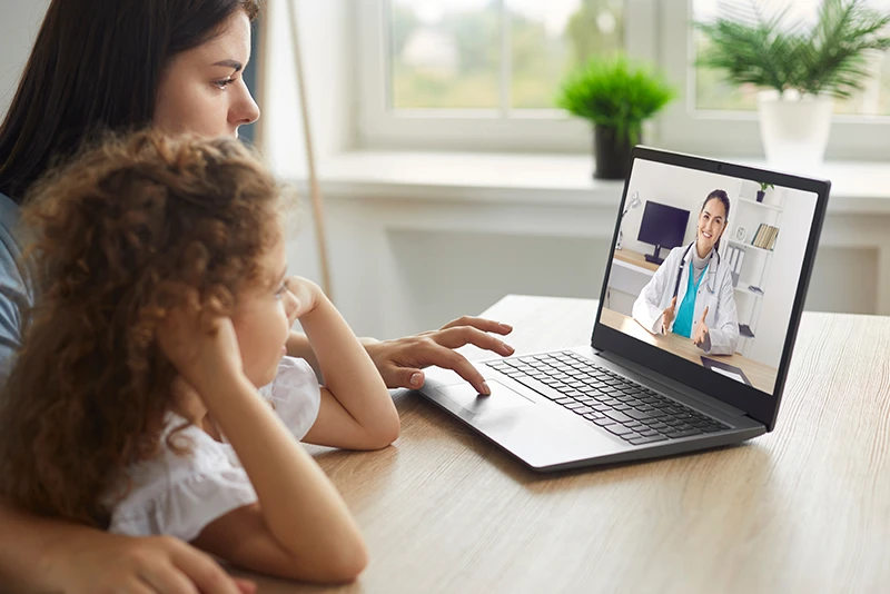 Mother and daughter having tele-health consultation with doctor on laptop