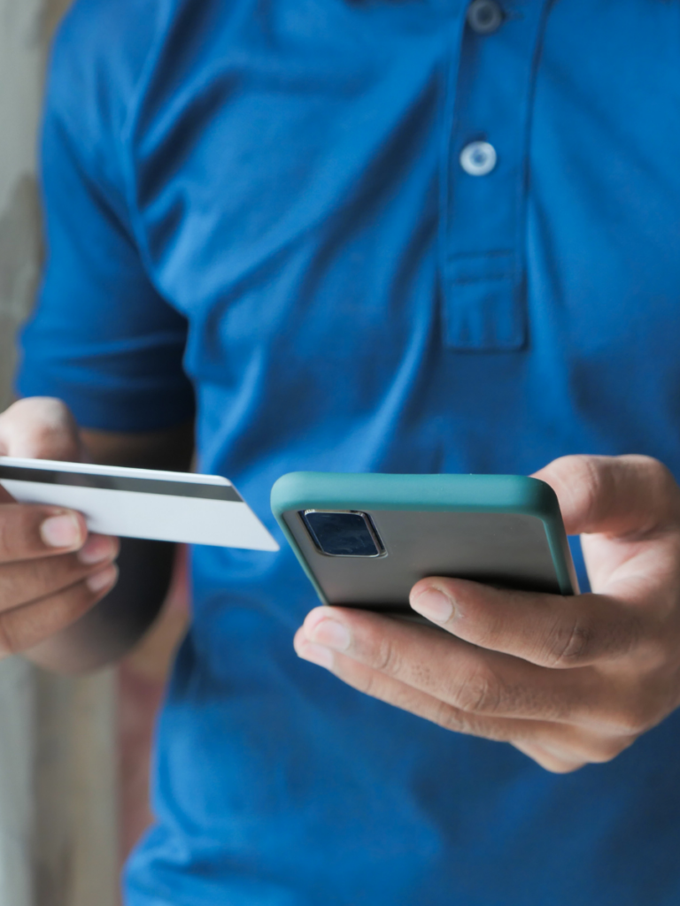 Person in blue golf shirt looking at smartphone and banking card.